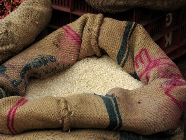 White rice grains spilling from a tan jute sack.