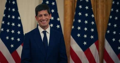 Kevin Warsh, former Federal Reserve governor, standing in front of multiple American flags.