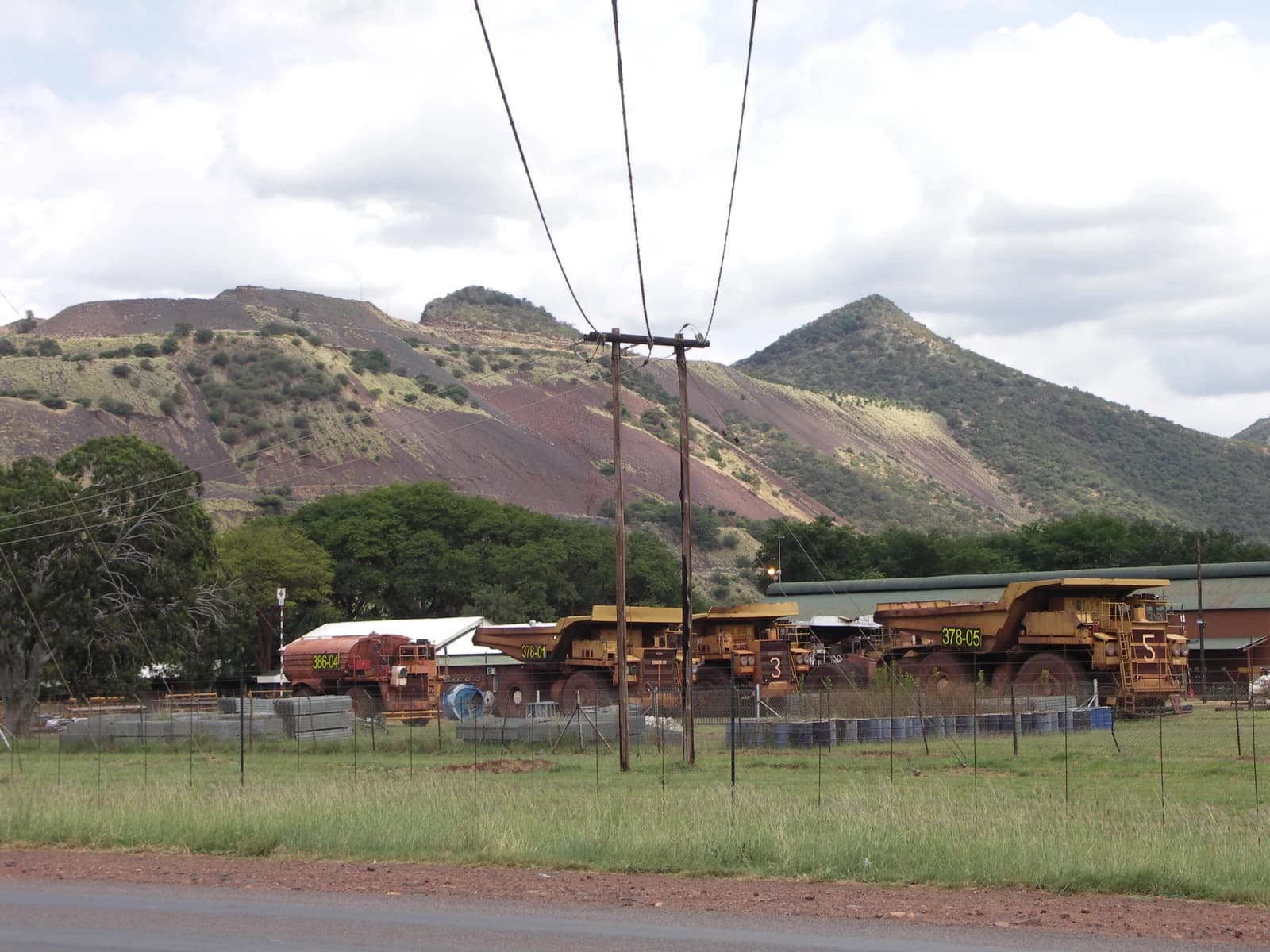Large yellow mining dump trucks parked in a yard with mountains in the background.