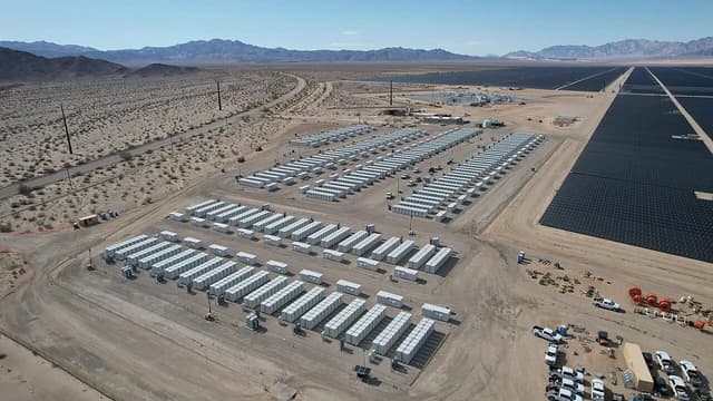 Aerial view of large battery energy storage system next to vast field of solar panels in a desert.