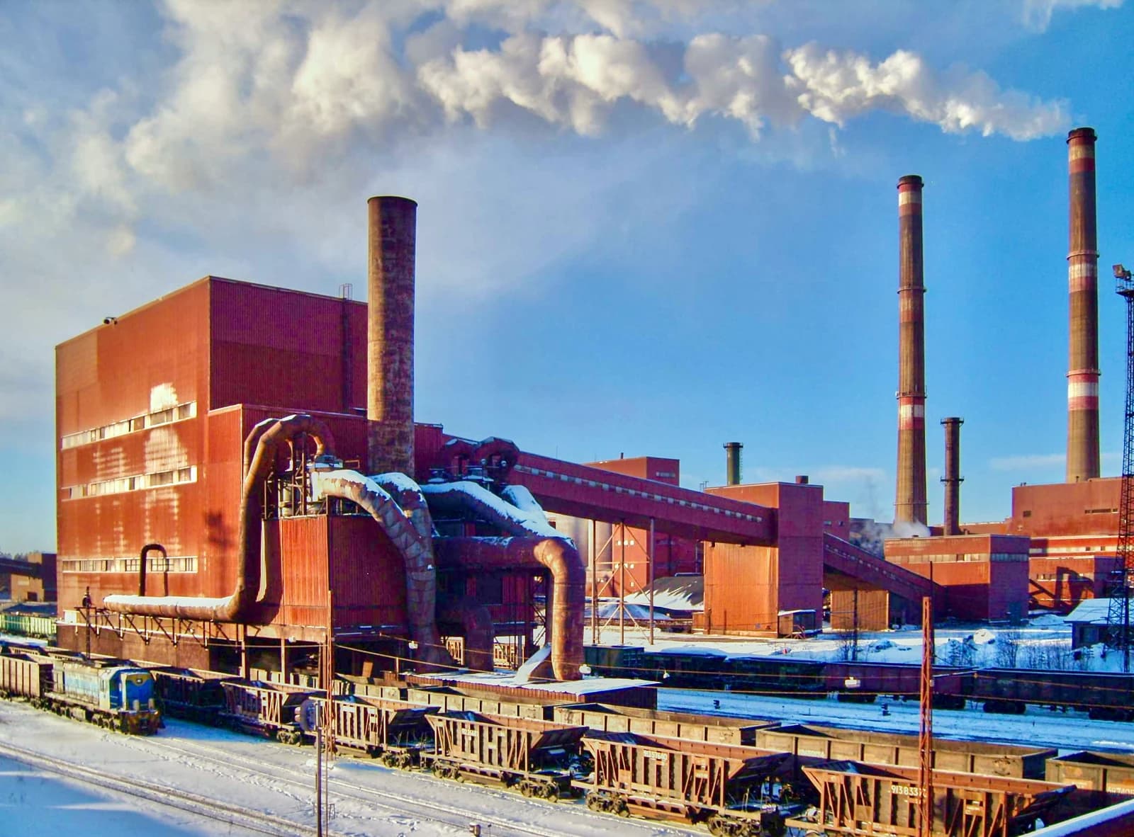Exterior view of the Karelsky Okatysh pelletizing plant with industrial buildings and train cars.