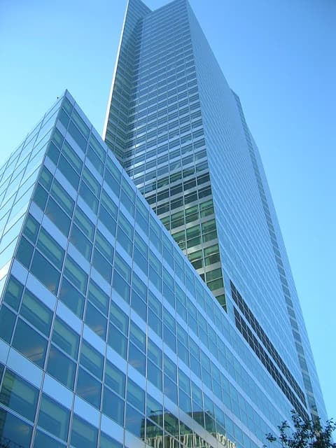 Exterior of Goldman Sachs headquarters, a modern glass skyscraper against a blue sky.
