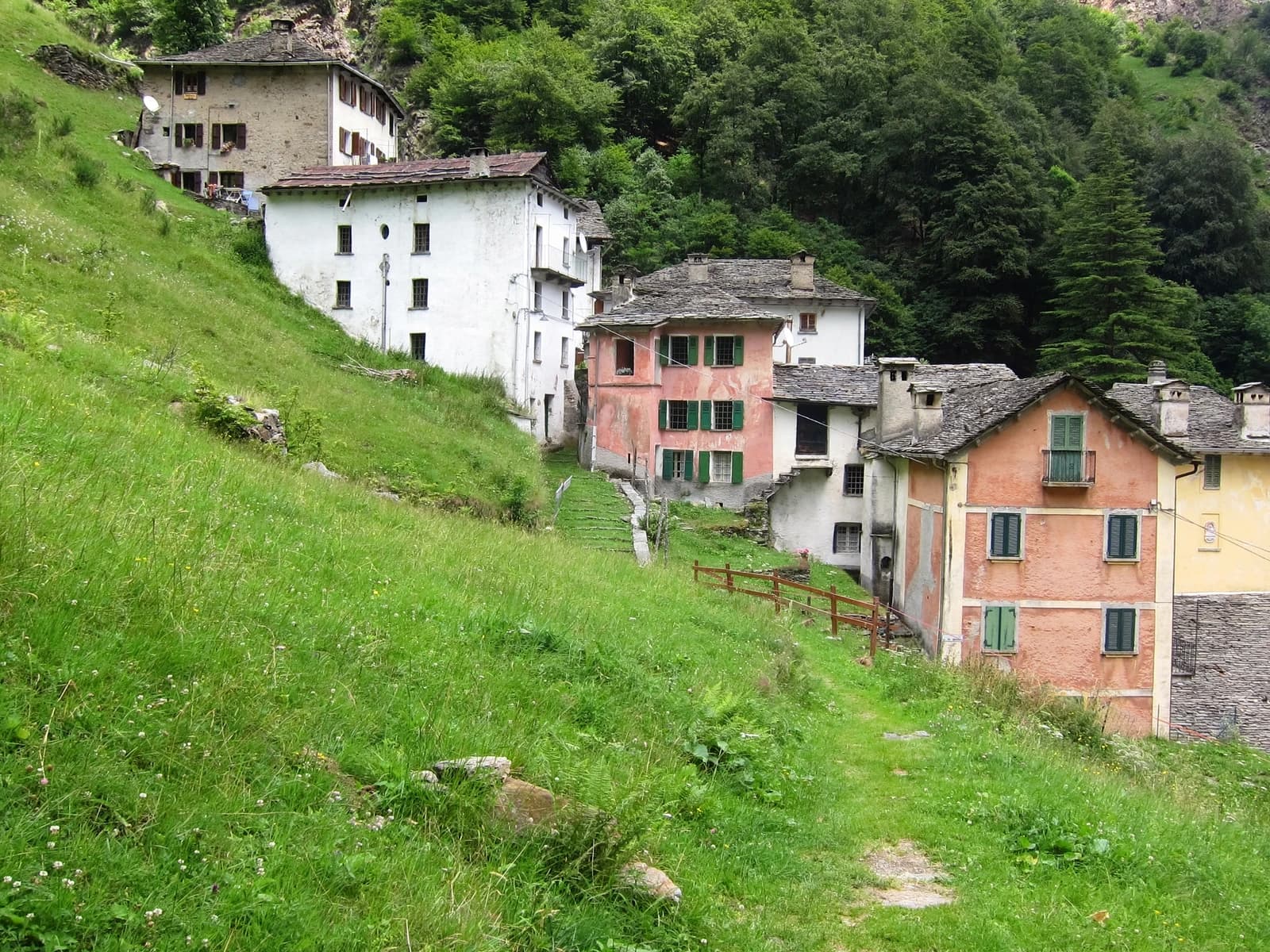 Colorful houses with green shutters nestled on a grassy hillside in a village.