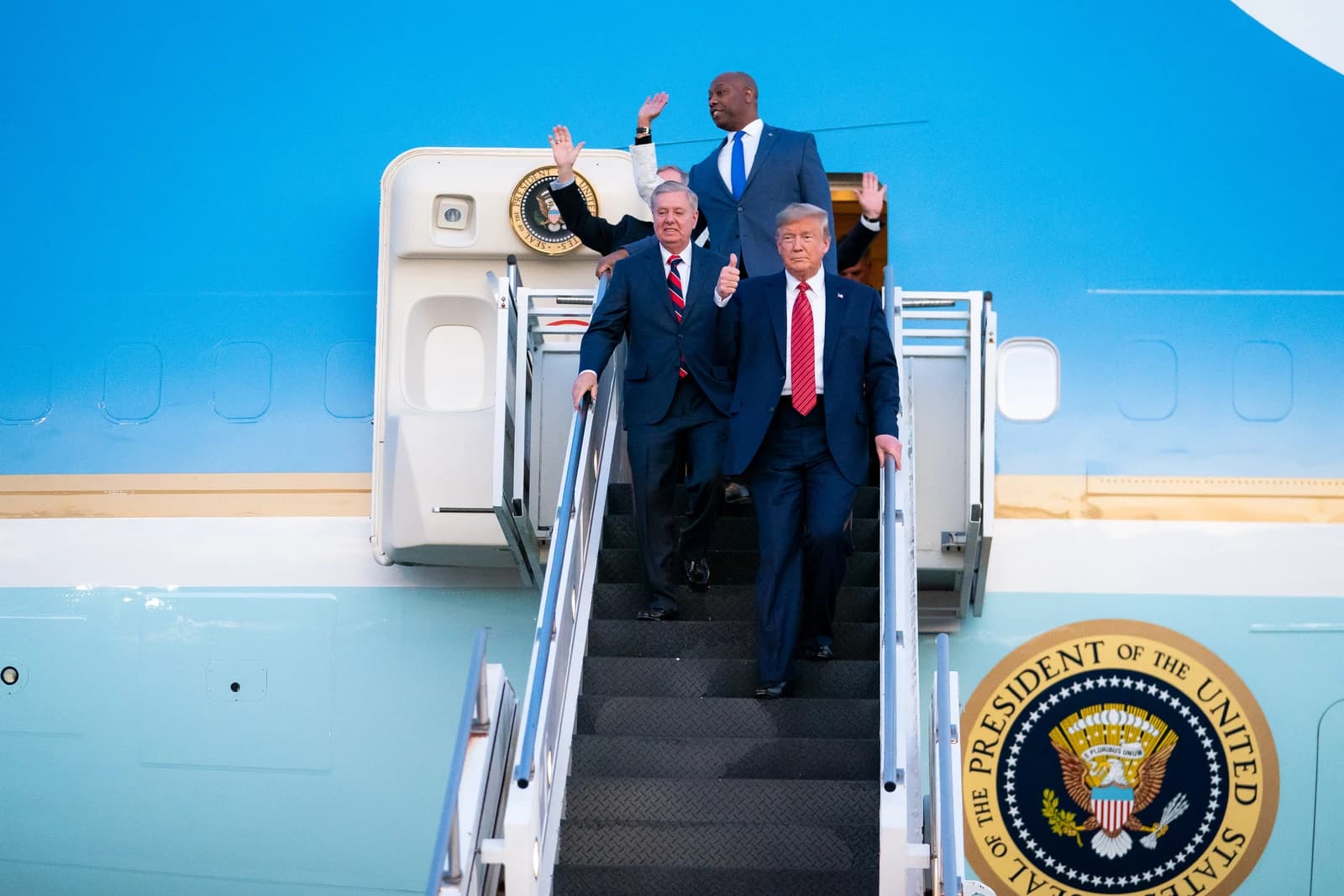 Donald Trump, President, and Lindsey Graham, Senator, walk down airplane stairs.
