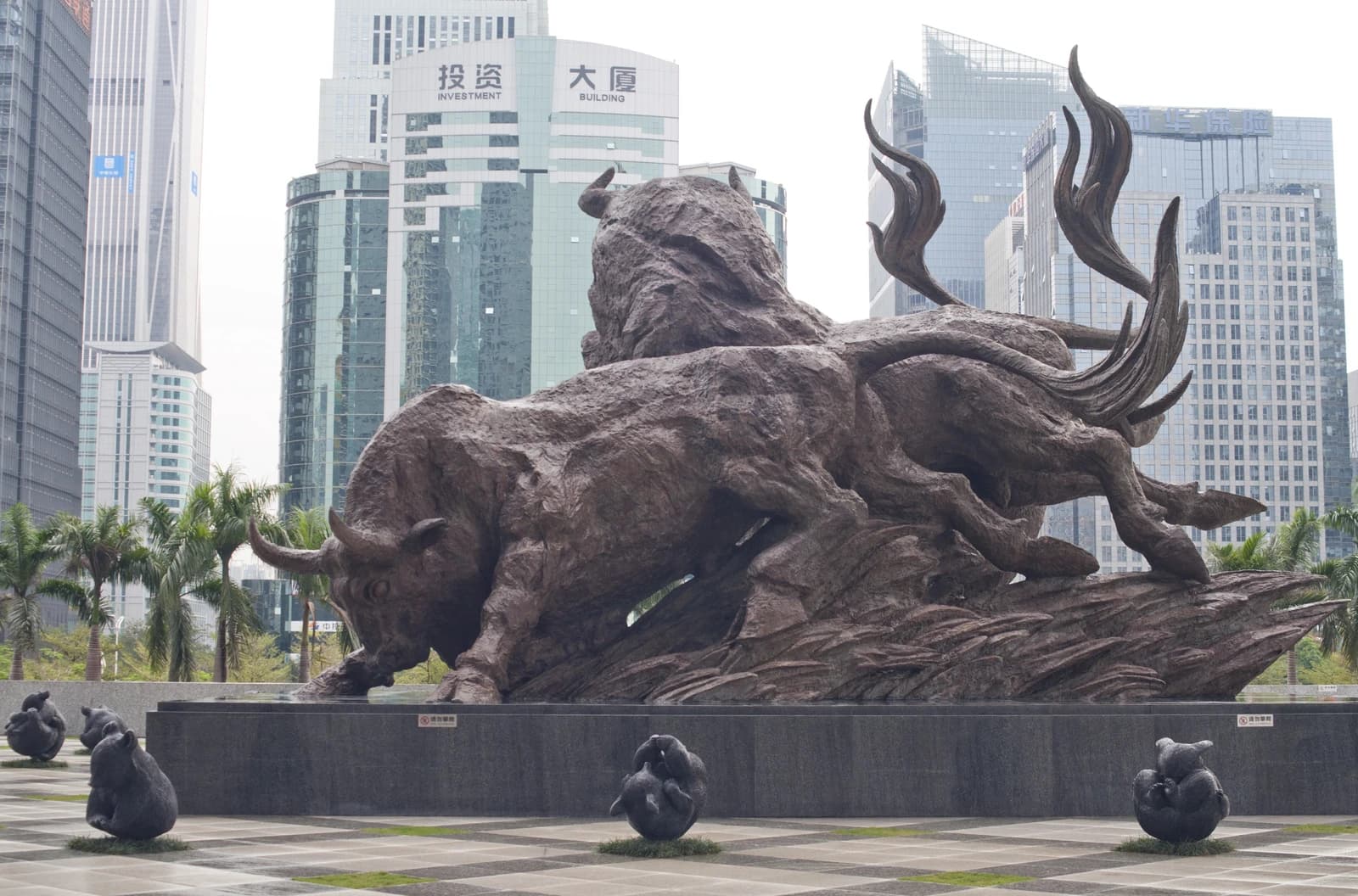Bronze bull sculpture with smaller bear sculptures in a city square.