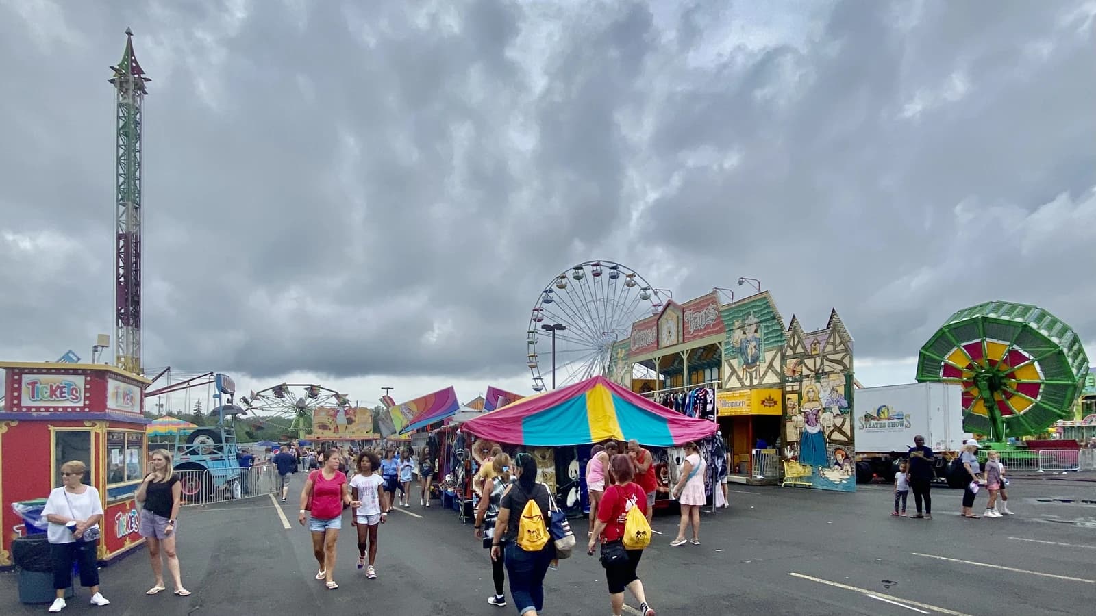 Fairgoers walk past amusement rides, games, and food stalls at a county fair.