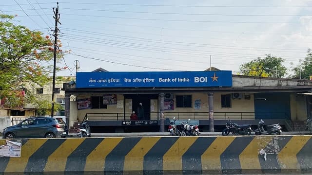 A Bank of India branch building with a blue sign, trees, and parked cars.