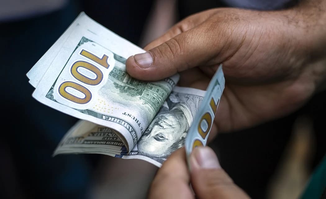 Close-up of a person's hands counting new one-hundred-dollar bills.