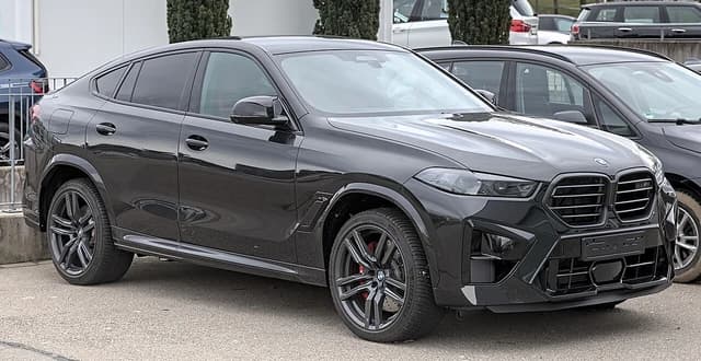 A black 2023 BMW X6 M (G06) parked outdoors, seen from the front three-quarters.