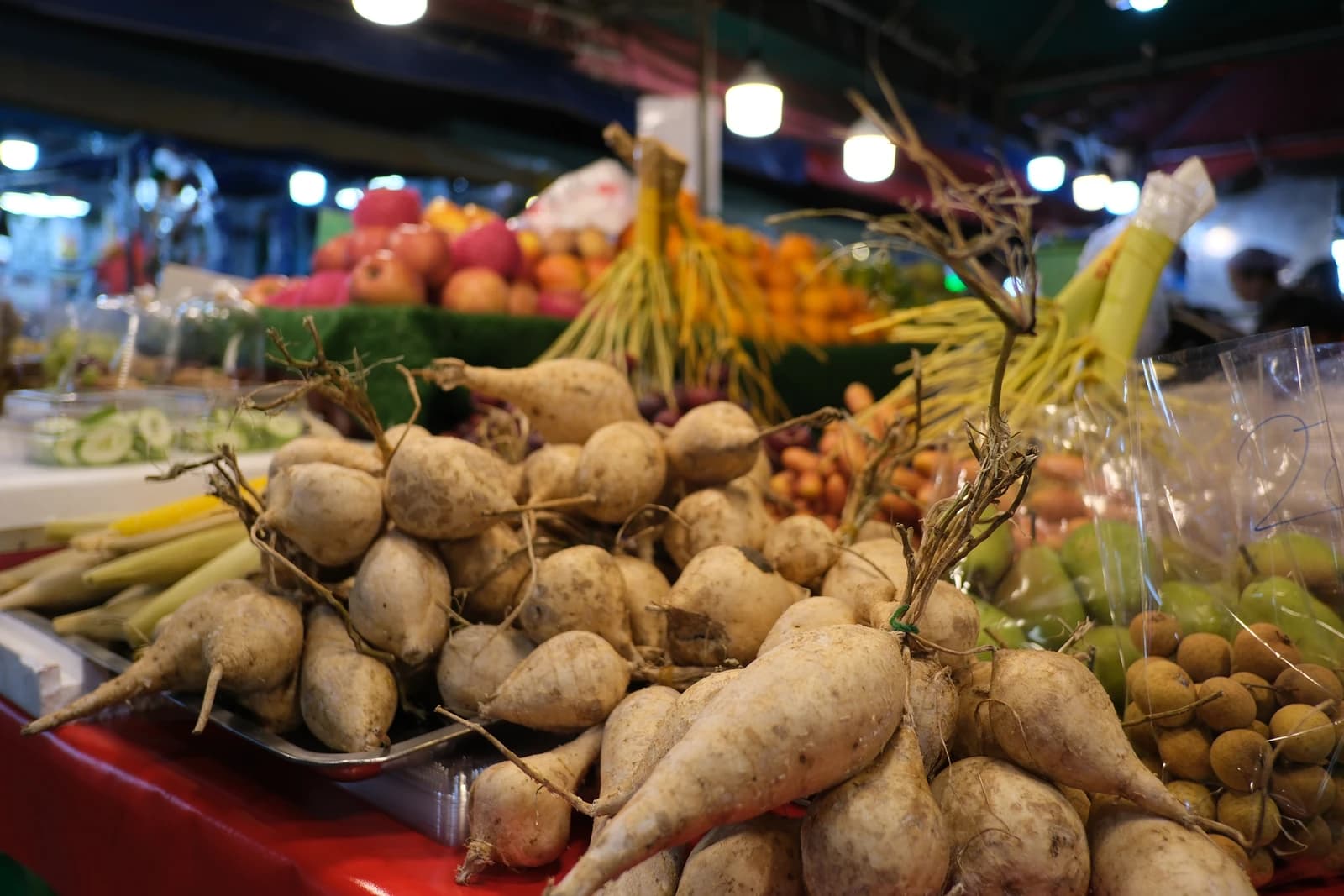 Fresh root vegetables are piled on a table at a bustling market stall.