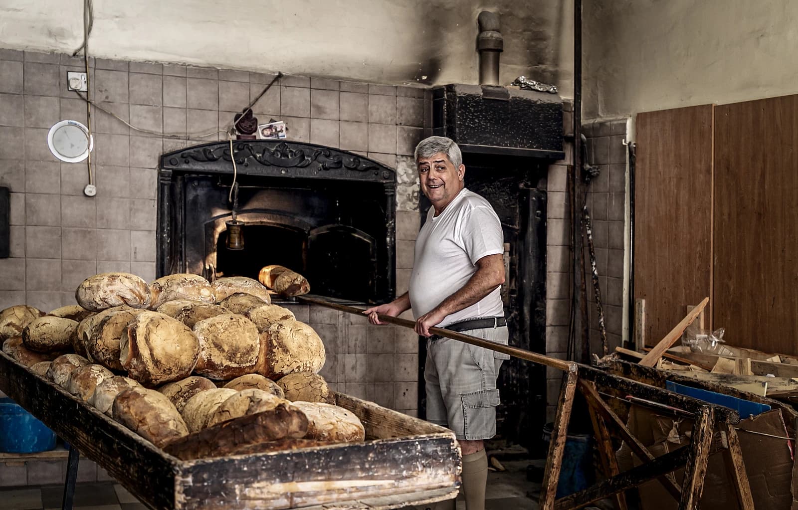 Baker using a long peel to put bread into a large, traditional stone oven.