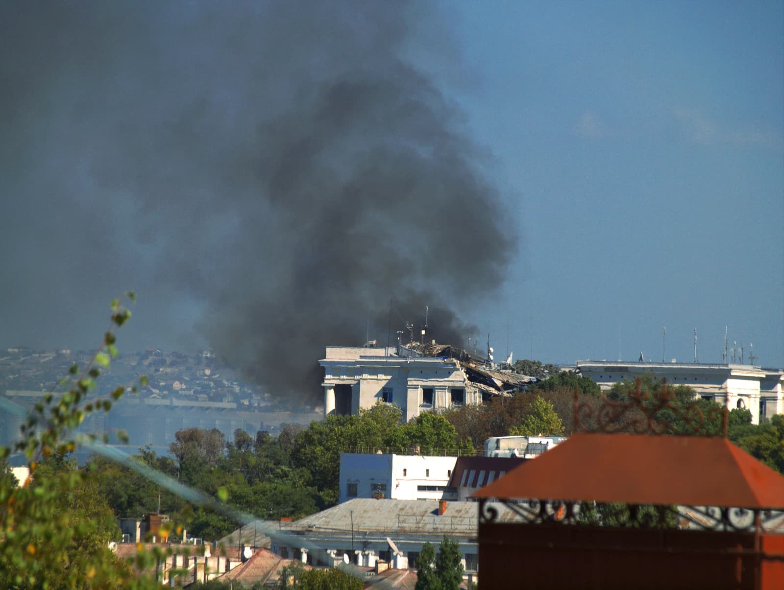 Damaged historic building of the Black Sea Fleet headquarters in Sevastopol, with smoke rising.