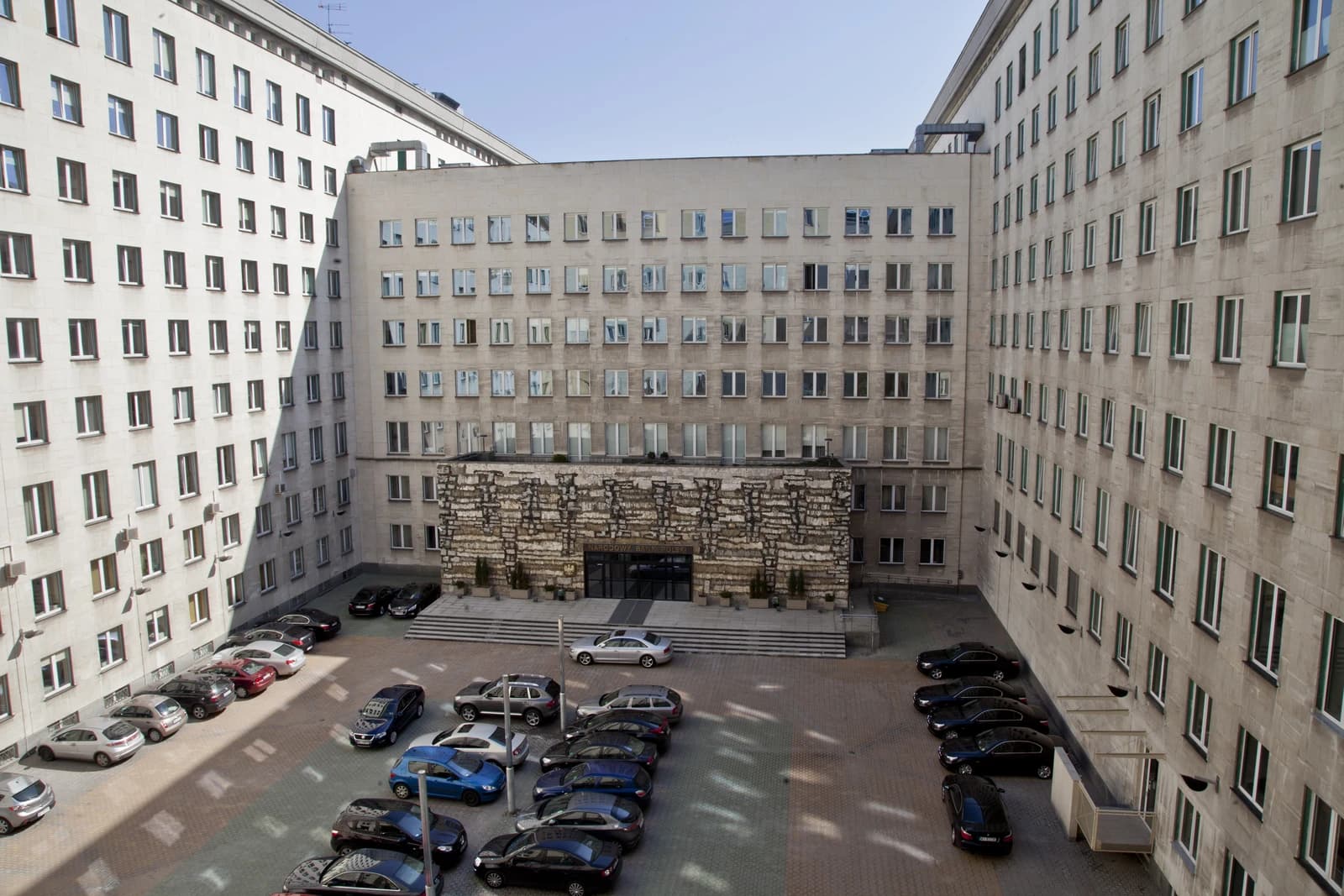 Exterior view of the National Bank of Poland headquarters building in Warsaw, with cars parked in the foreground.