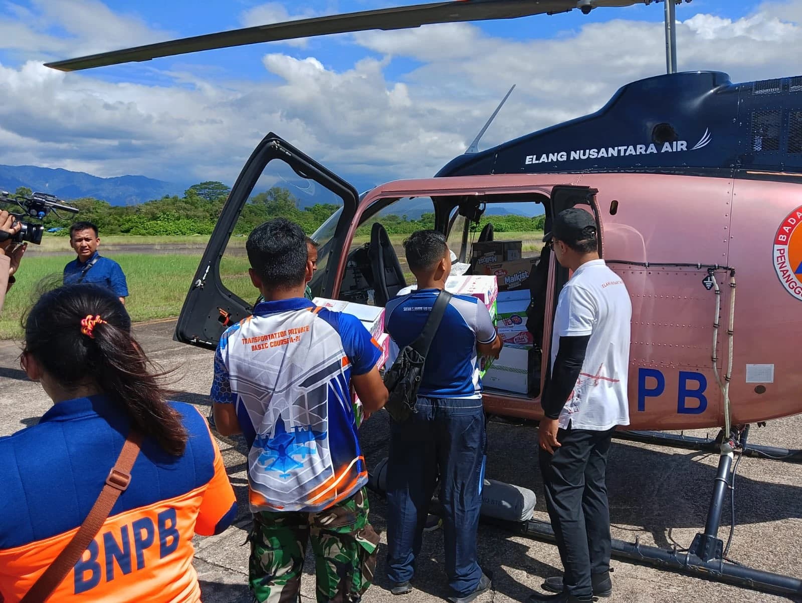 People load boxes of aid supplies into a pink Bell 505 helicopter.