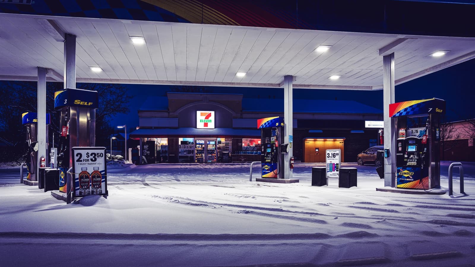 7-Eleven gas station in winter with snow covering the ground at night.