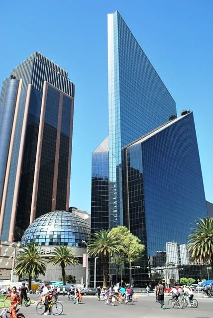 Mexico City Stock Exchange building with modern architecture, palm trees, and people on bicycles.