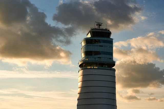 An air traffic control tower stands tall against a partly cloudy sky.