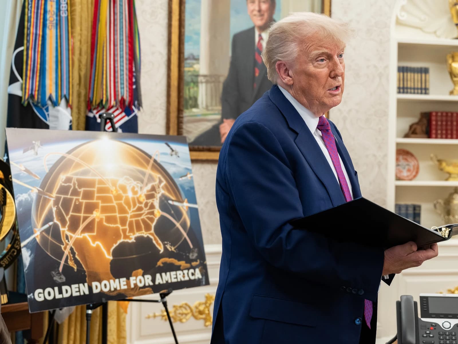 Donald Trump in the Oval Office, standing beside a display board.