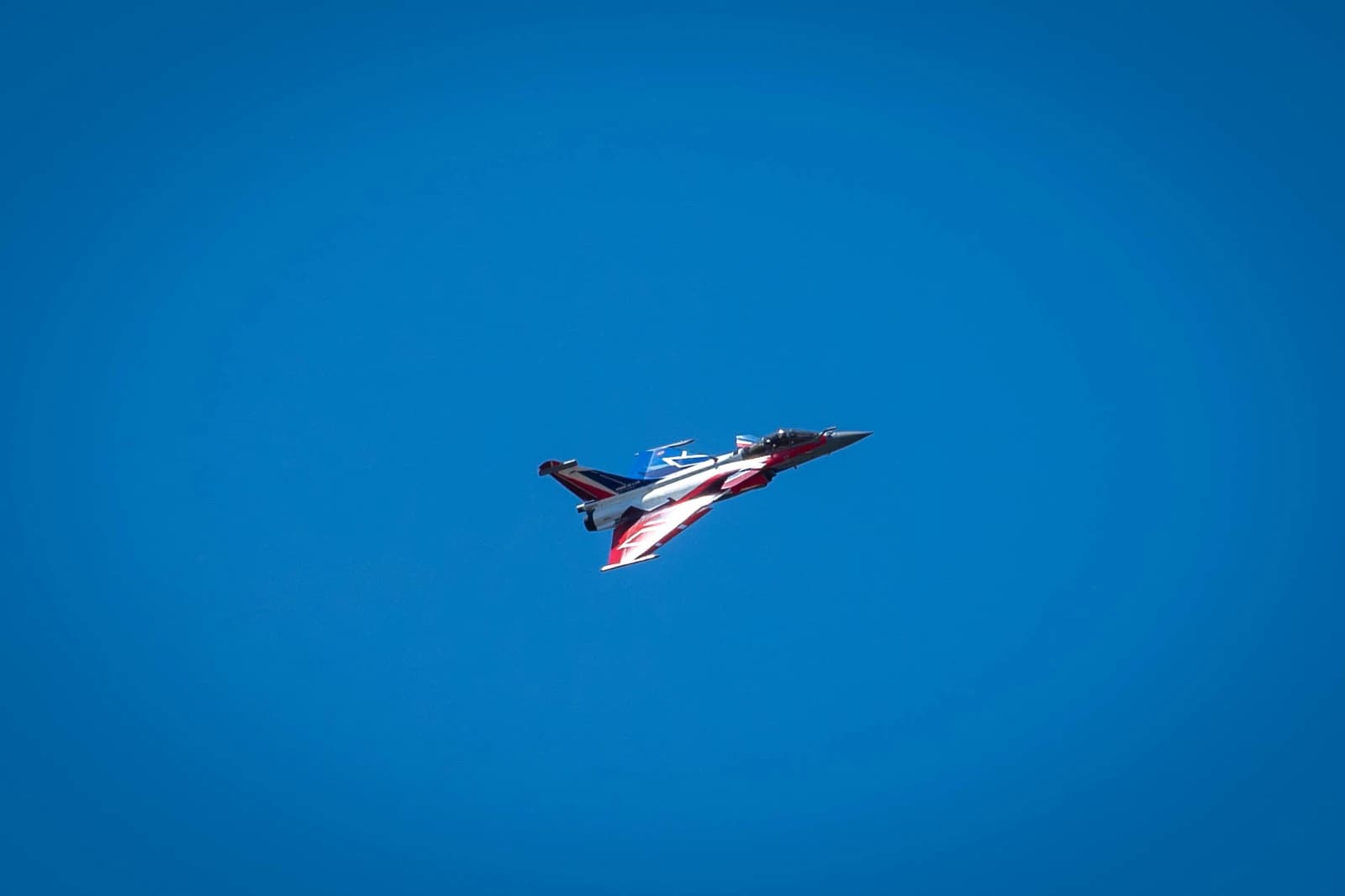 Rafale fighter jet with red, white, and blue markings in a clear blue sky.