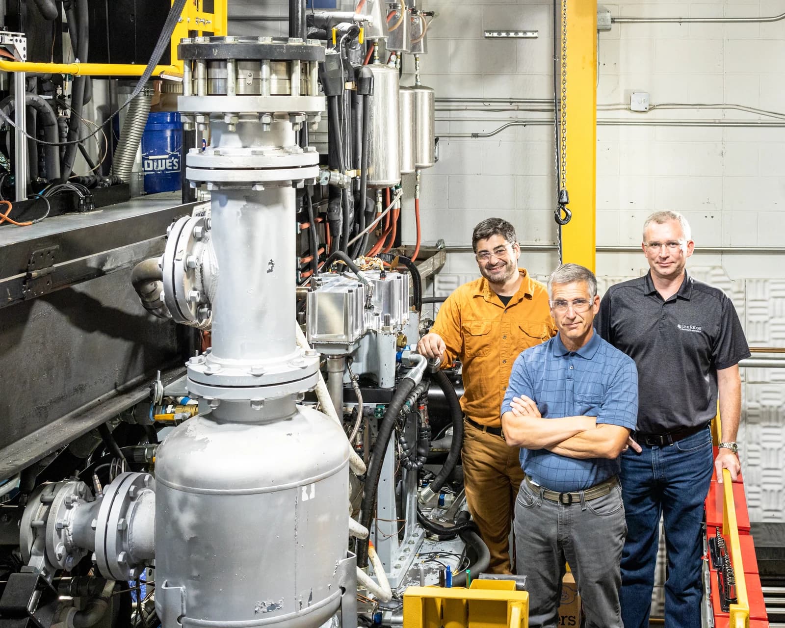 Three engineers stand next to an ExxonMobil marine engine in a workshop.