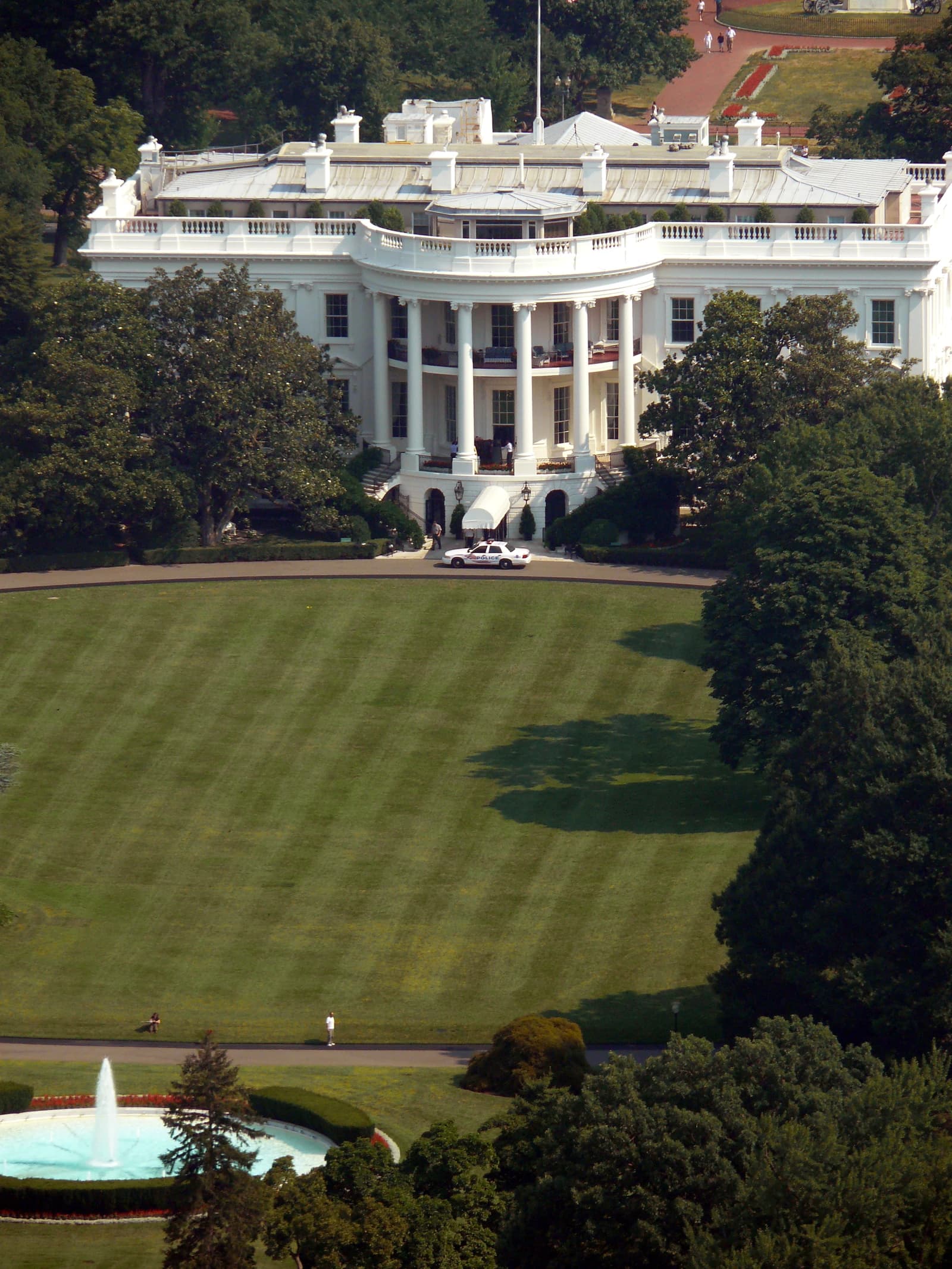 Aerial view of the White House south facade with a police car in front.