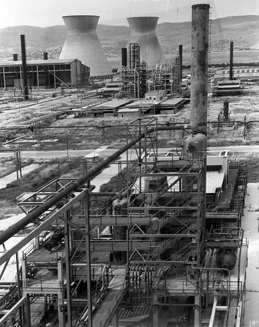 An aerial view of oil refineries in Haifa, Israel, featuring industrial structures and large cooling towers.