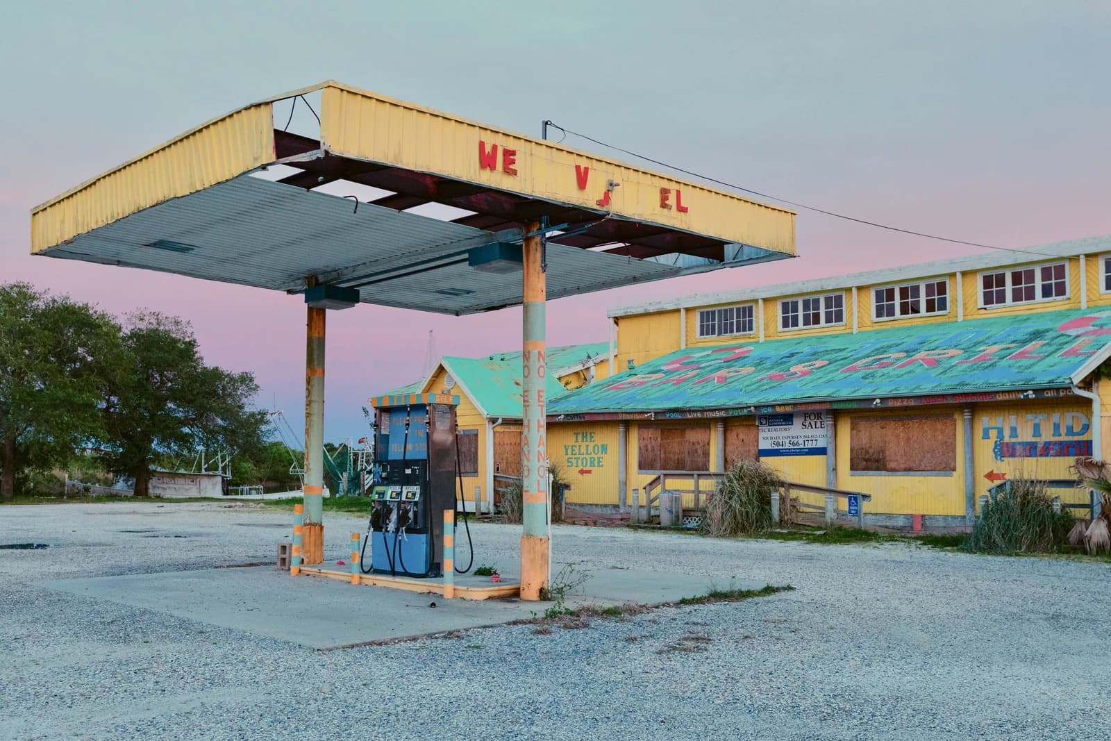 Closed gas station with boarded-up windows and 'For Sale' sign in New Orleans.