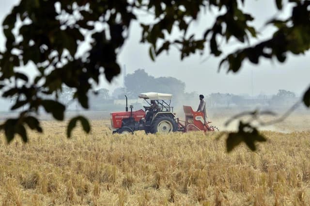 Farmer operating a red tractor with a field preparation attachment in Punjab, India.