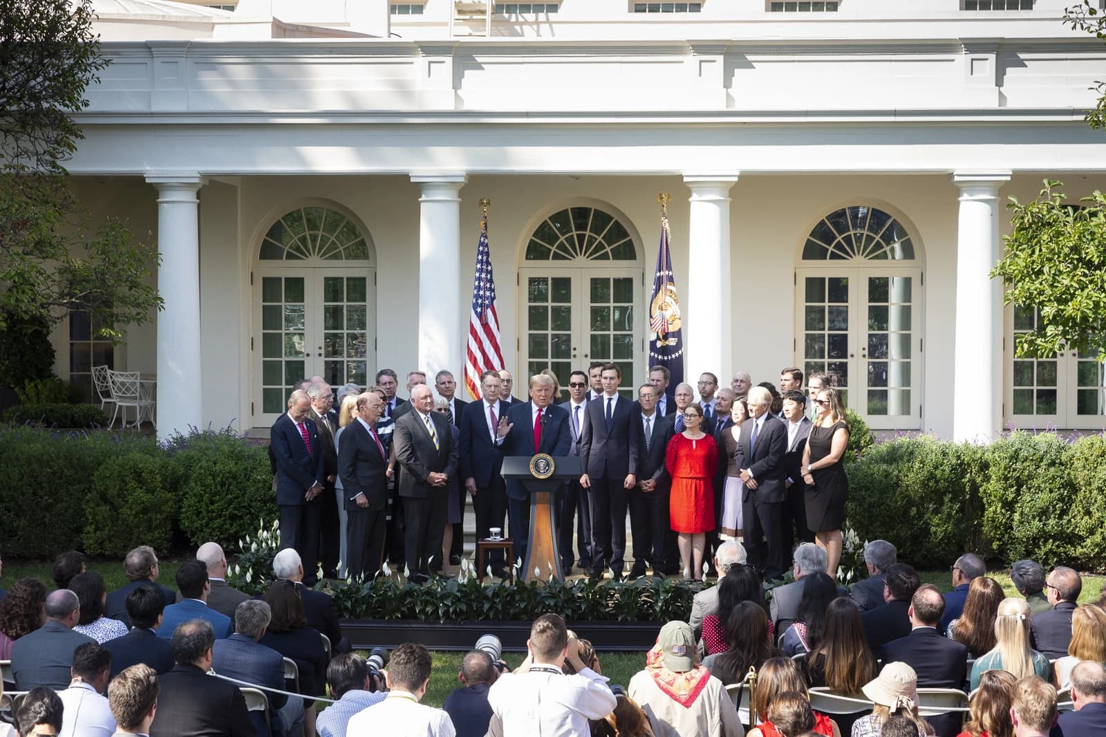 President Donald Trump speaks at a podium in the Rose Garden, surrounded by officials.