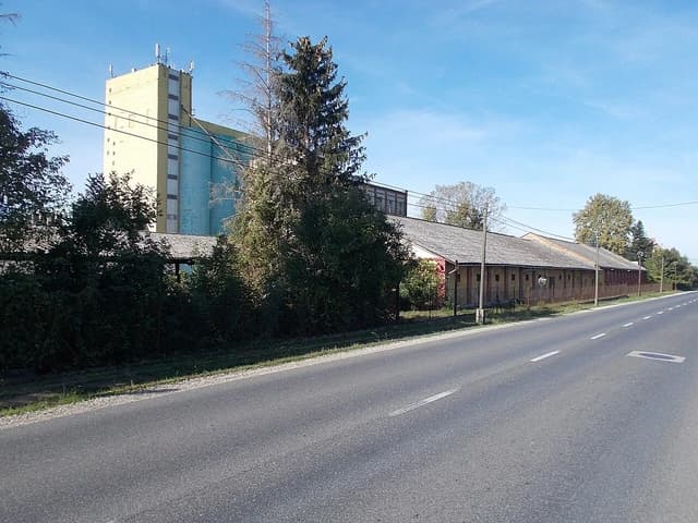 Roadside view of a large grain storage facility in Enying, Hungary, under a clear sky.
