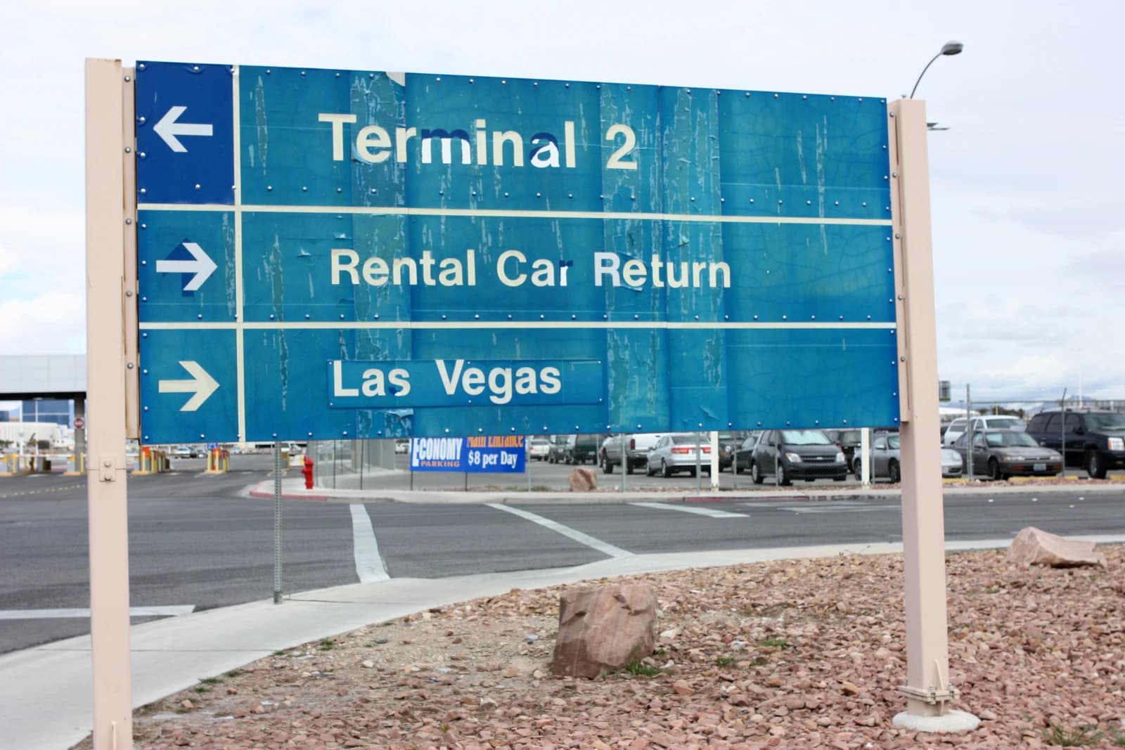 A blue road sign pointing to Terminal 2, Rental Car Return, and Las Vegas.