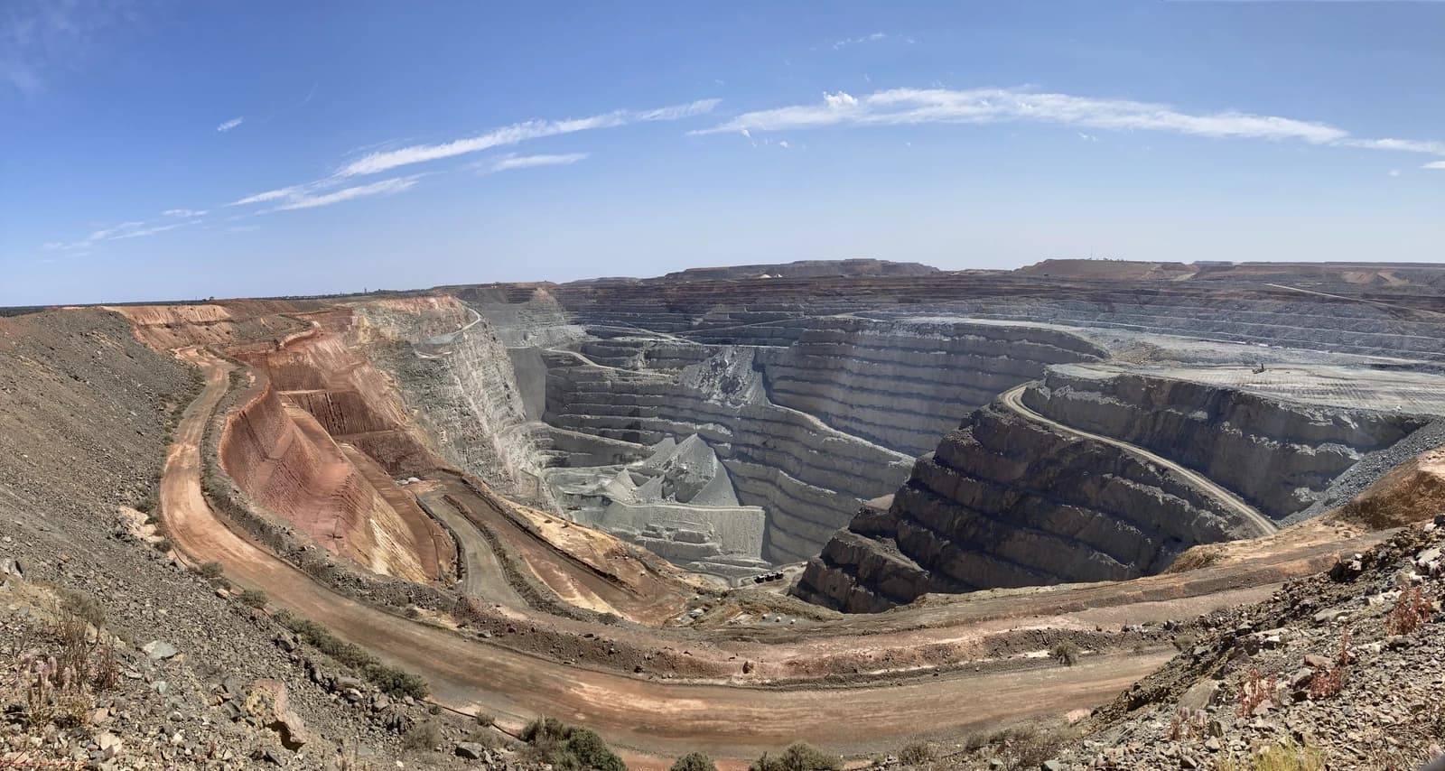 An expansive view of the Kalgoorlie Super Pit, an open-cut gold mine, under a blue sky.