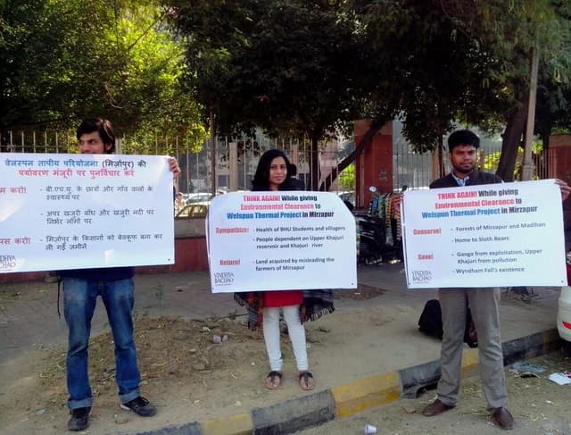 Three environmental activists holding protest signs in Delhi.