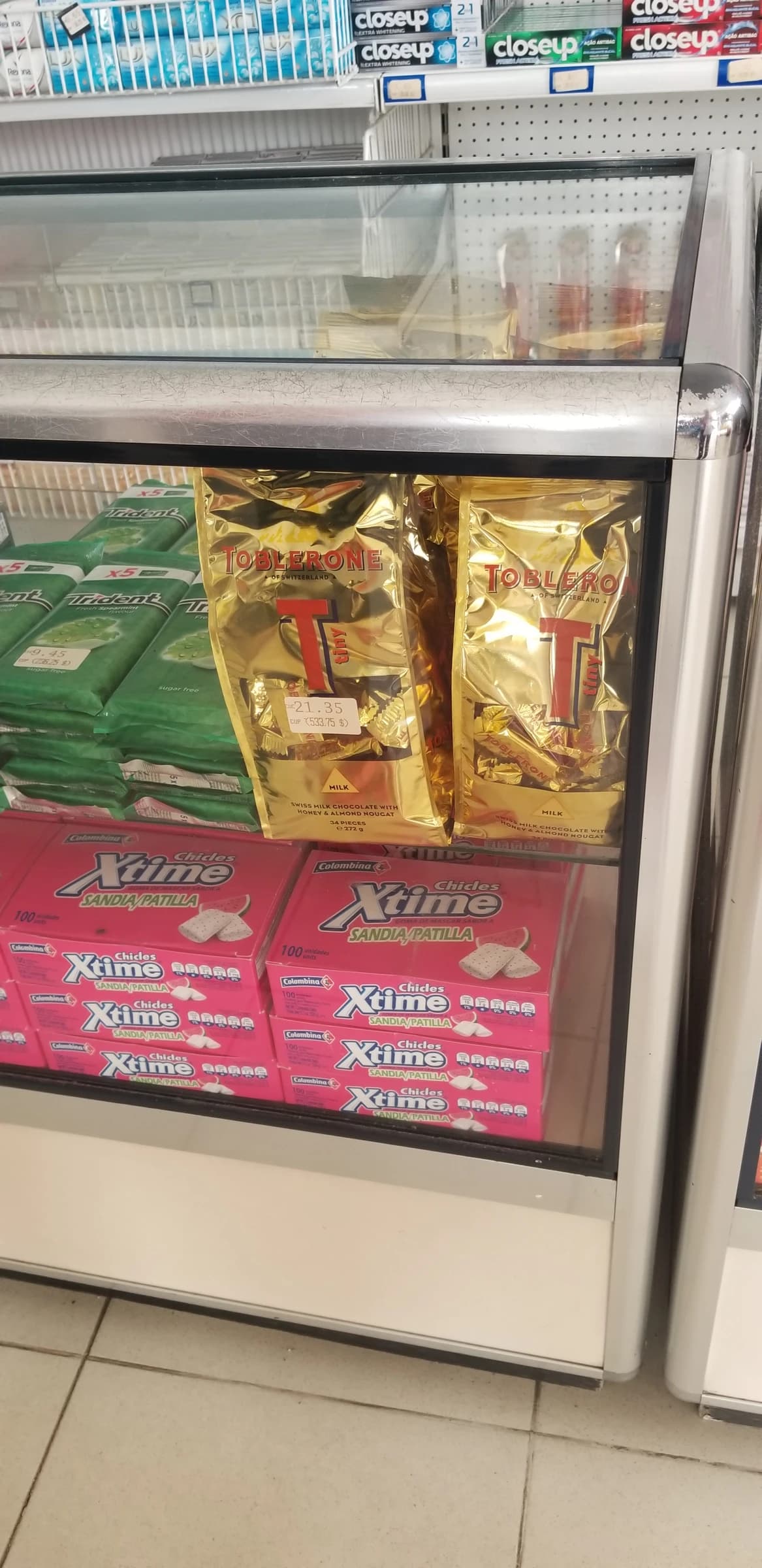 Toblerone chocolates and various gums displayed on shelves inside a supermarket refrigerated display case.