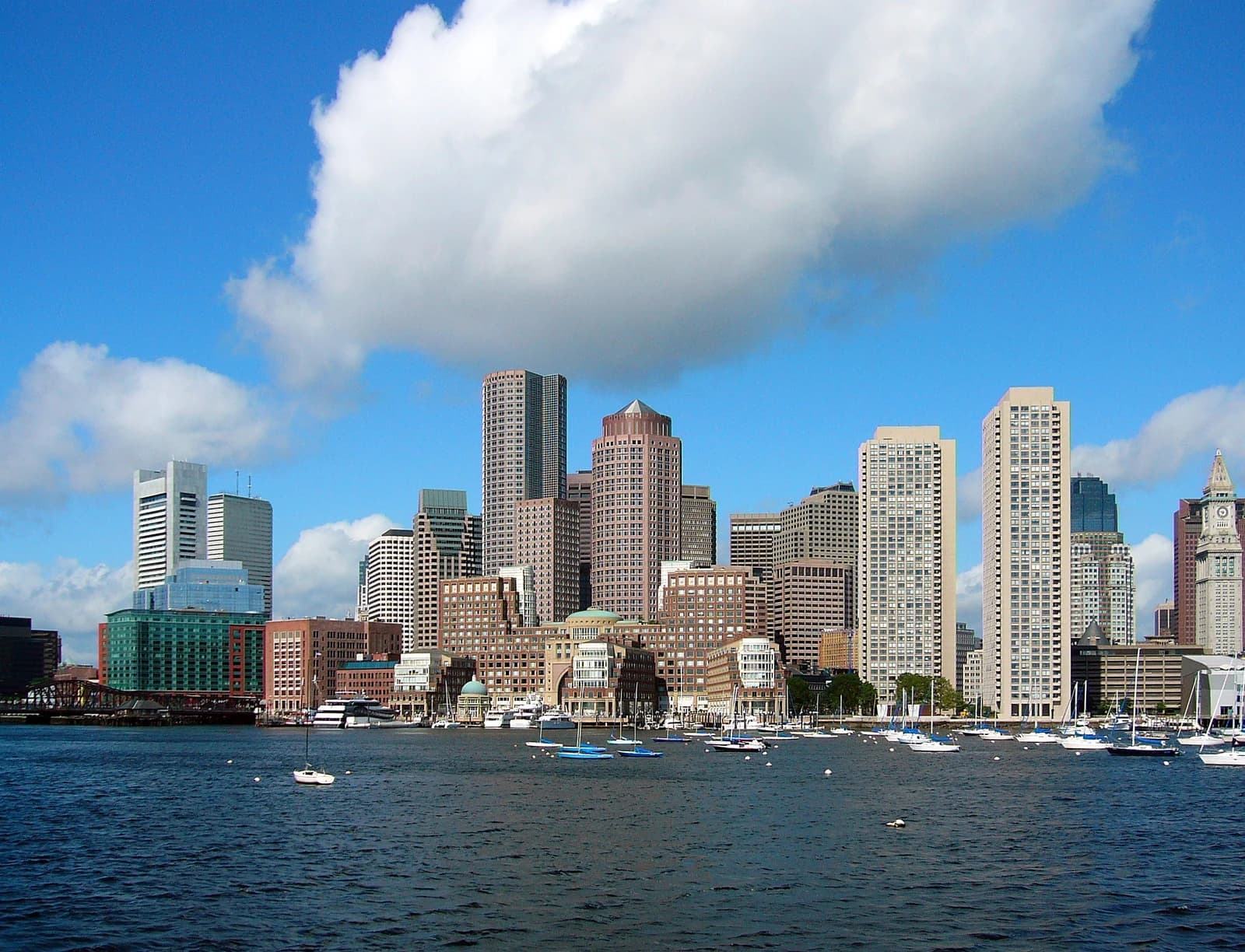 Boston Financial District skyline featuring multiple tall buildings and a body of water with boats.