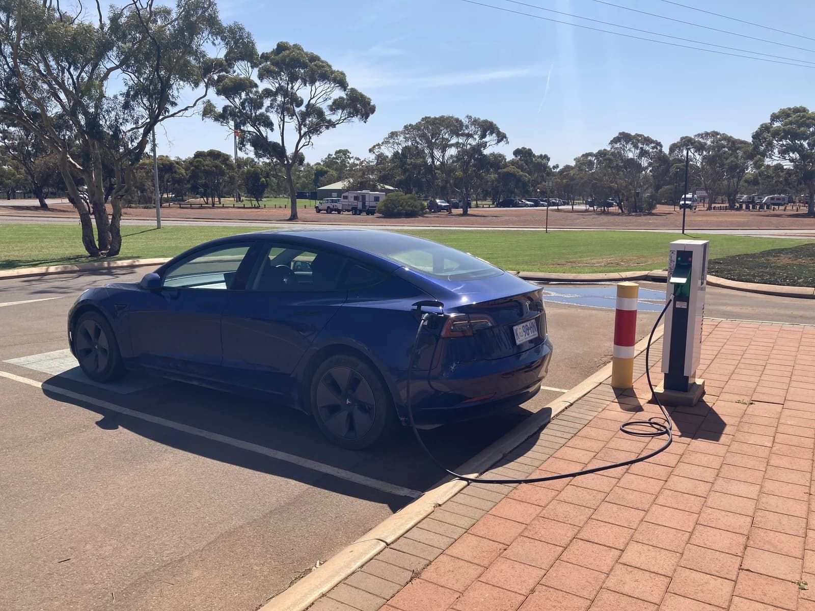 Blue Tesla Model 3 car parked and charging at an AC station.
