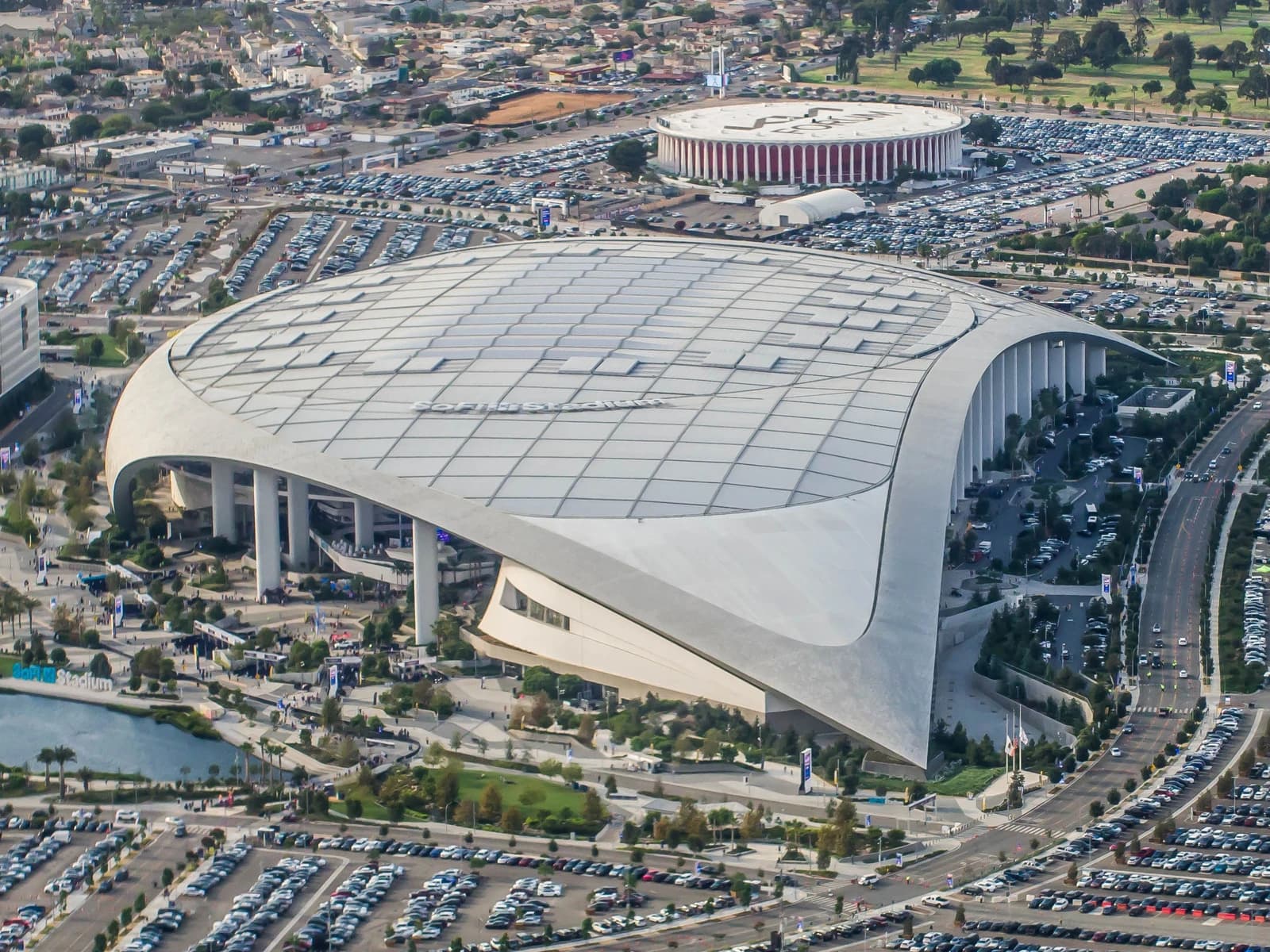 Aerial view of SoFi Stadium in Inglewood, California, surrounded by parking lots and urban landscape.