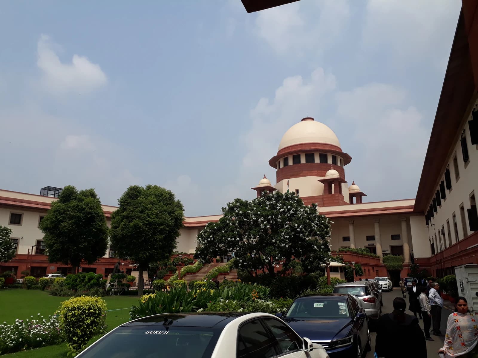 Exterior view of the Supreme Court of India building with cars and people outside.