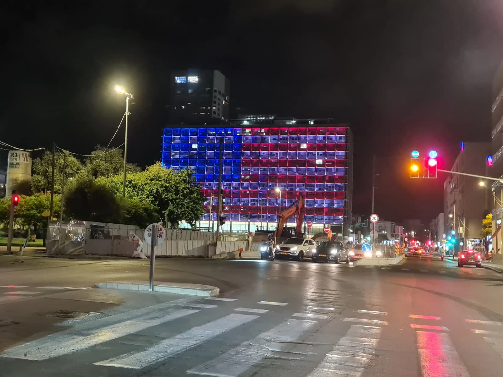 Tel Aviv Municipality building illuminated in red, white, and blue at night.