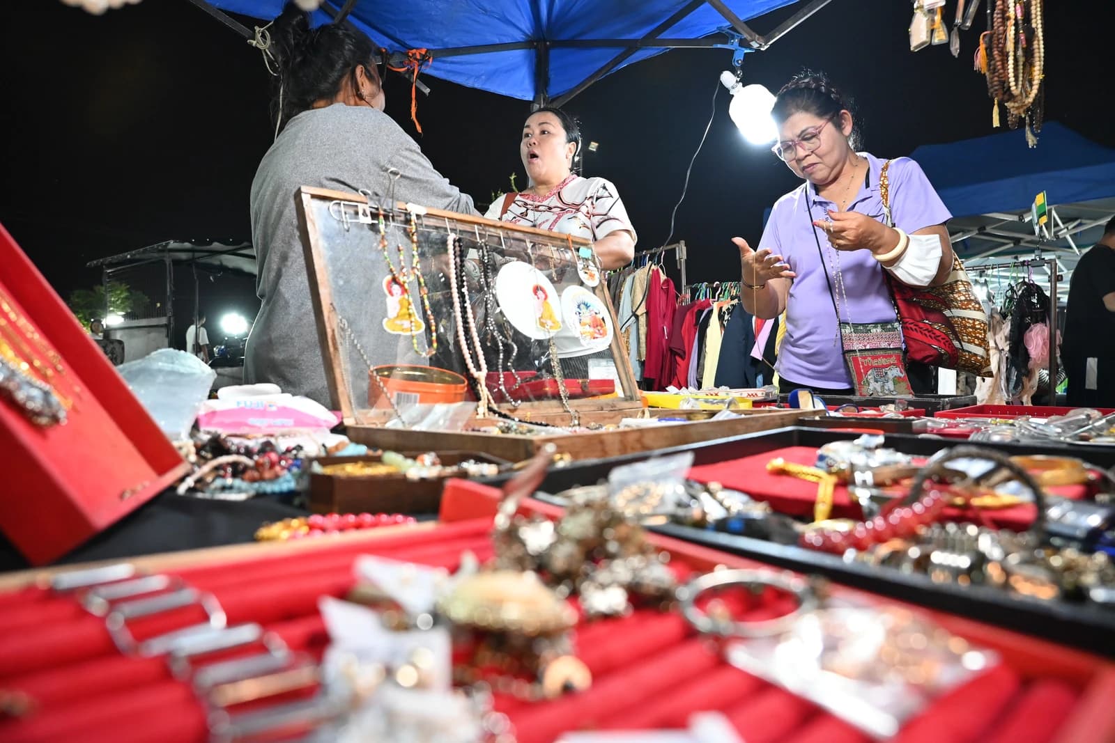 Customers browsing jewelry at a night market stand under canopy lights.