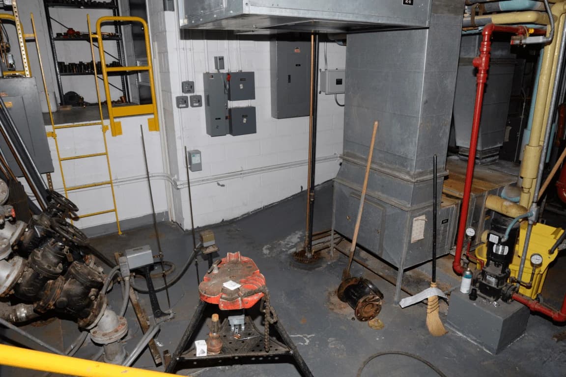 An industrial room contains machinery, pipes, electrical panels, and various tools.