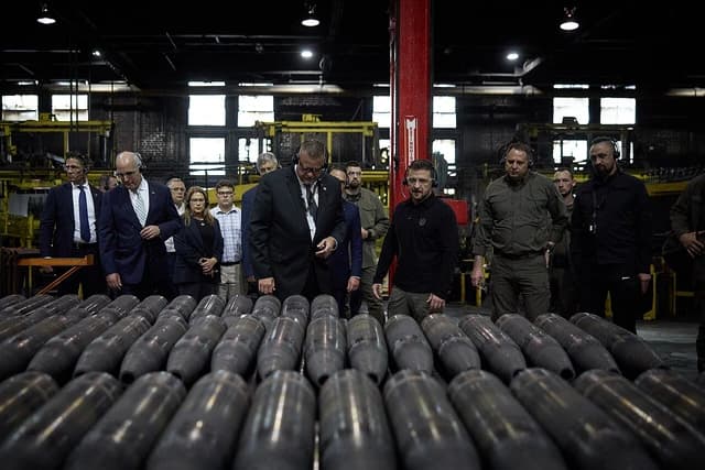President Zelensky and officials tour a factory floor with artillery shells.