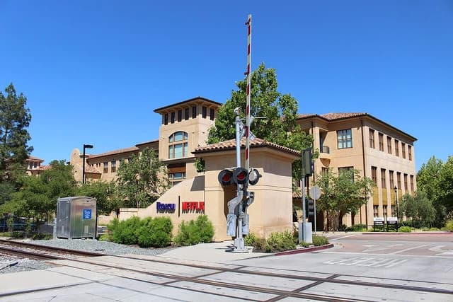 Building with a prominent sign for Roku and Netflix near railway tracks.