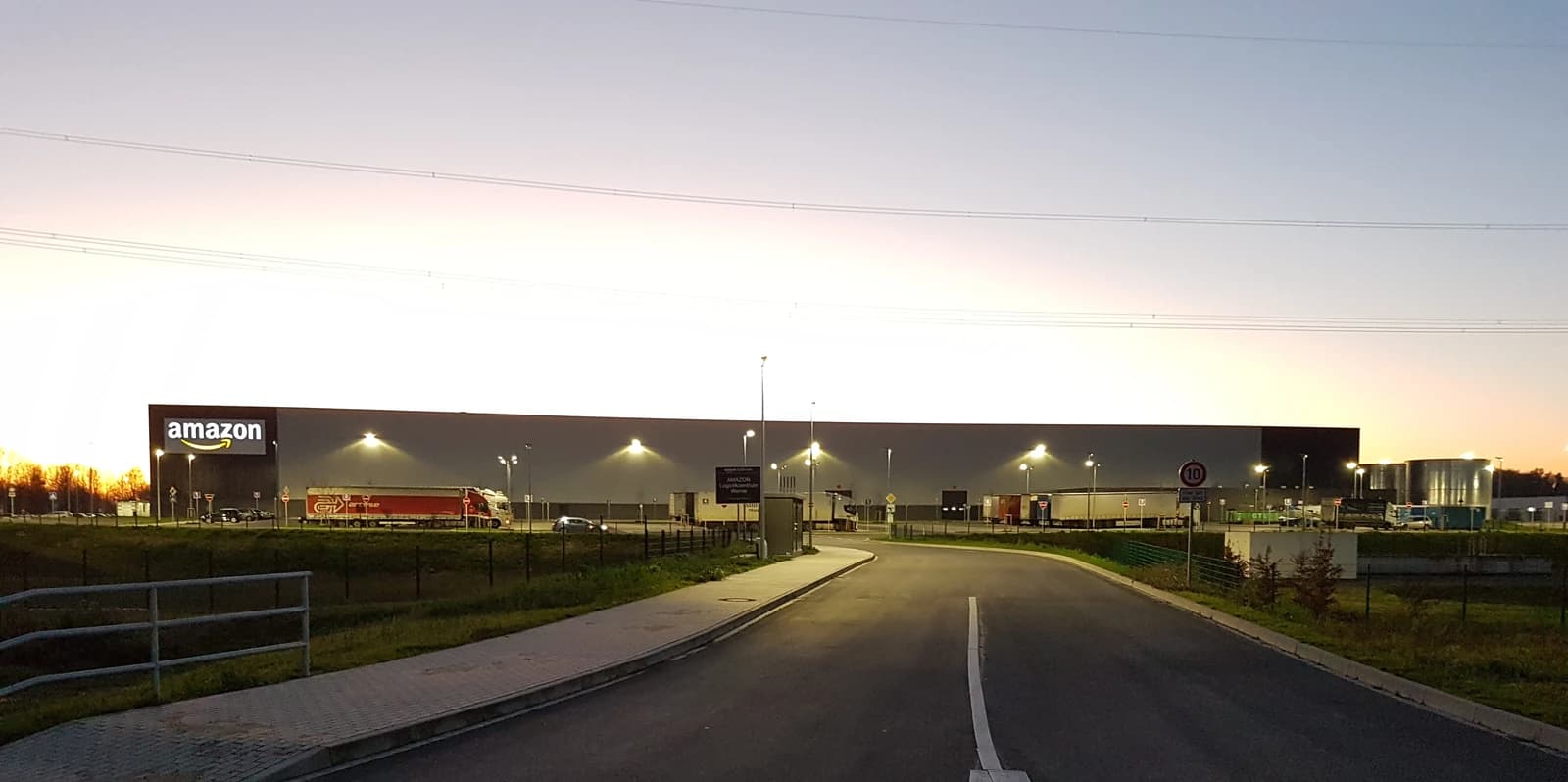 Amazon logistics center in Werne at dusk, with trucks and streetlights visible.