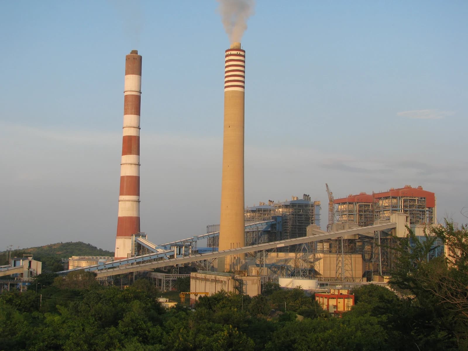 An NTPC thermal power plant featuring two large smokestacks, one actively emitting smoke.