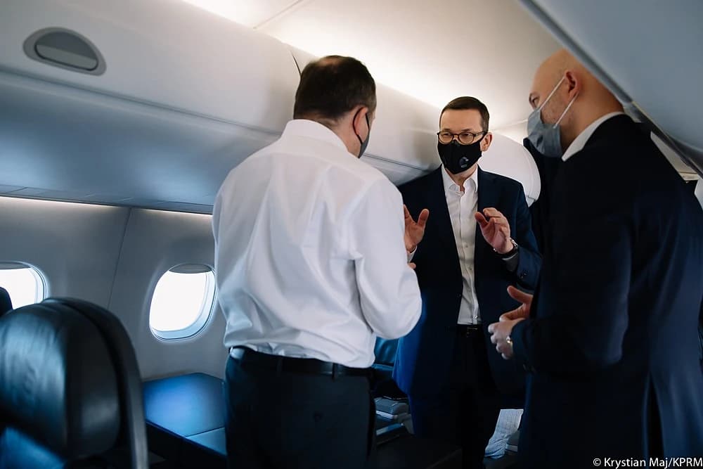 Mateusz Morawiecki, Prime Minister of Poland, speaks with two men on an airplane.