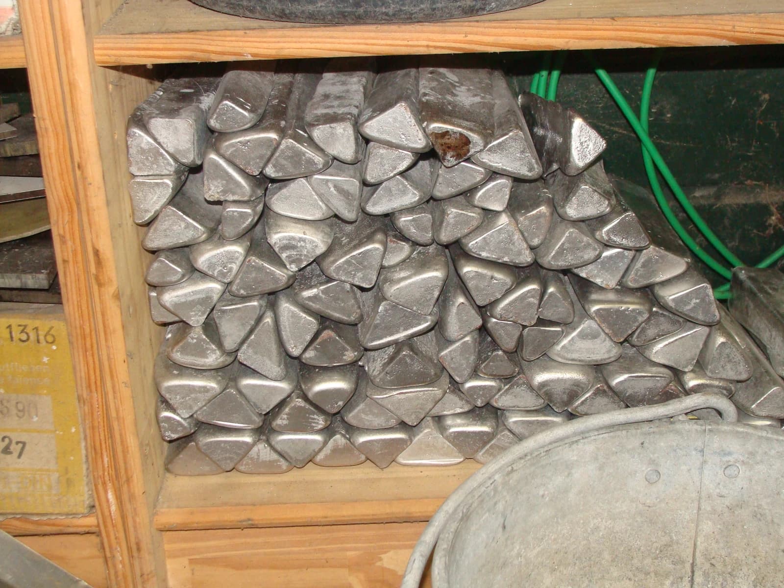 Stack of triangular aluminum ingots on wooden shelves in a storage area.