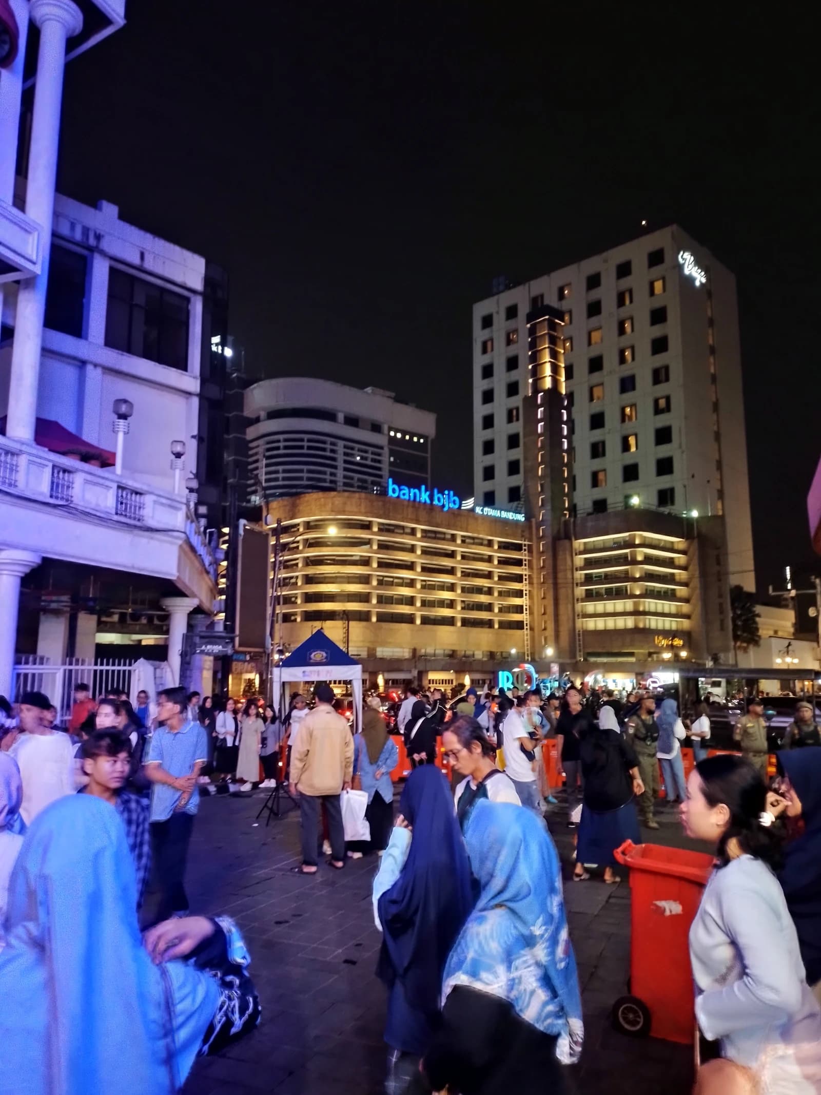 Bank BJB Headquarters building illuminated at night in Bandung, Indonesia, with people walking in the foreground.