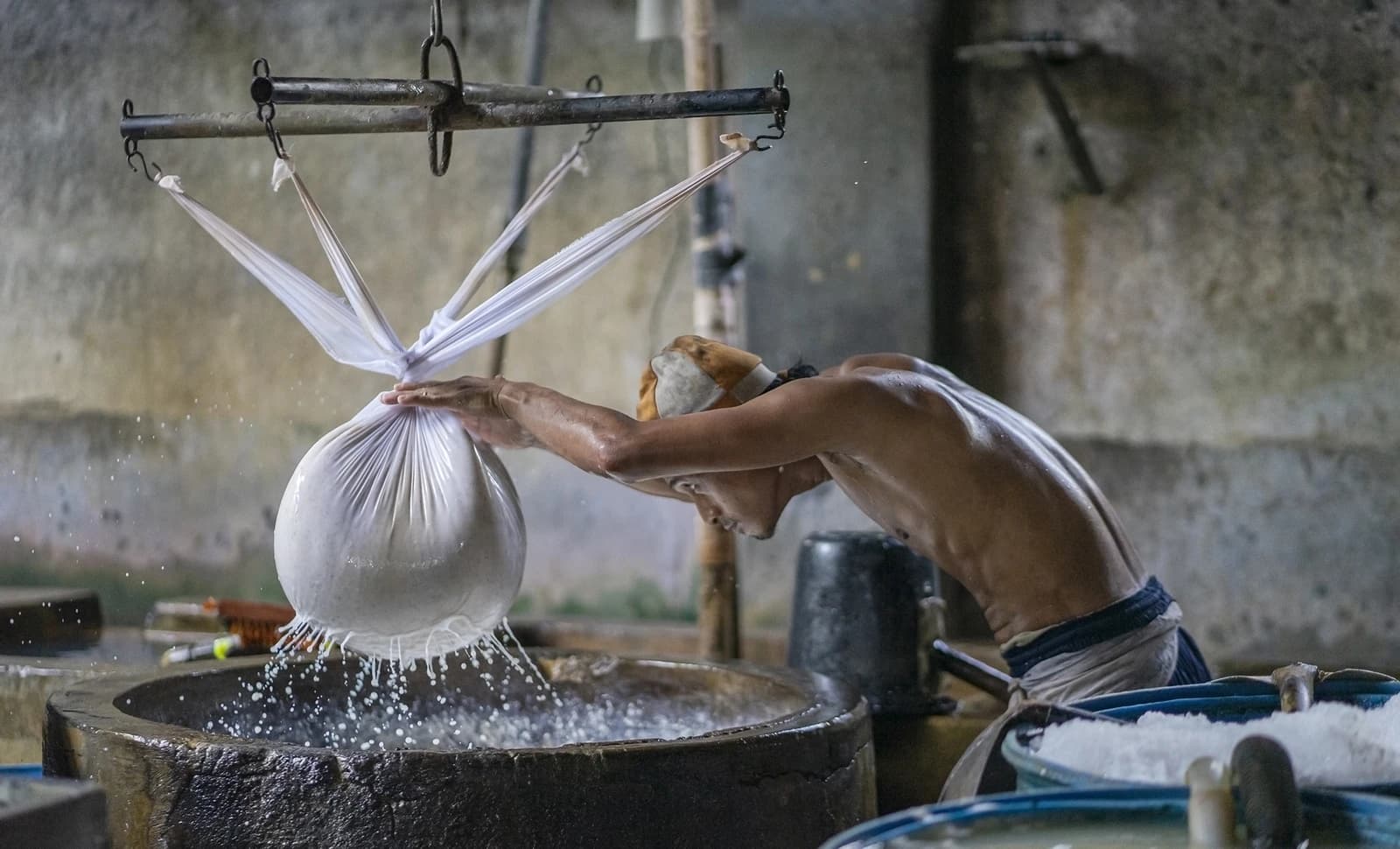 Craftsman pressing soybeans in a cloth bag over a large stone basin.
