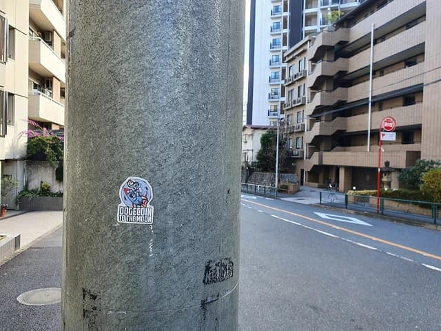 Dogecoin 'to the moon' sticker attached to a gray utility pole in Tokyo.